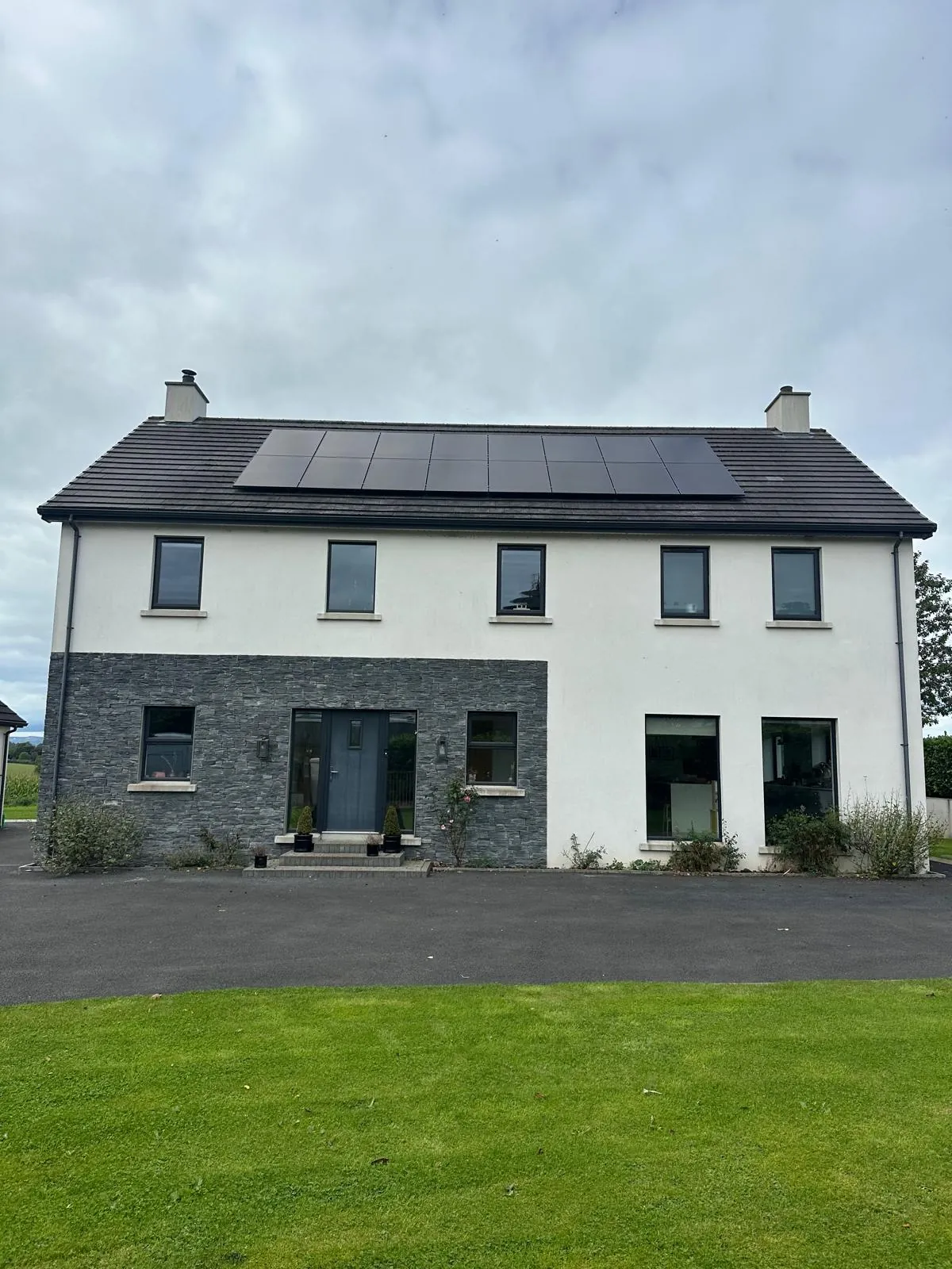 Two rows of black solar panels on a two-storey white and stone-clad home