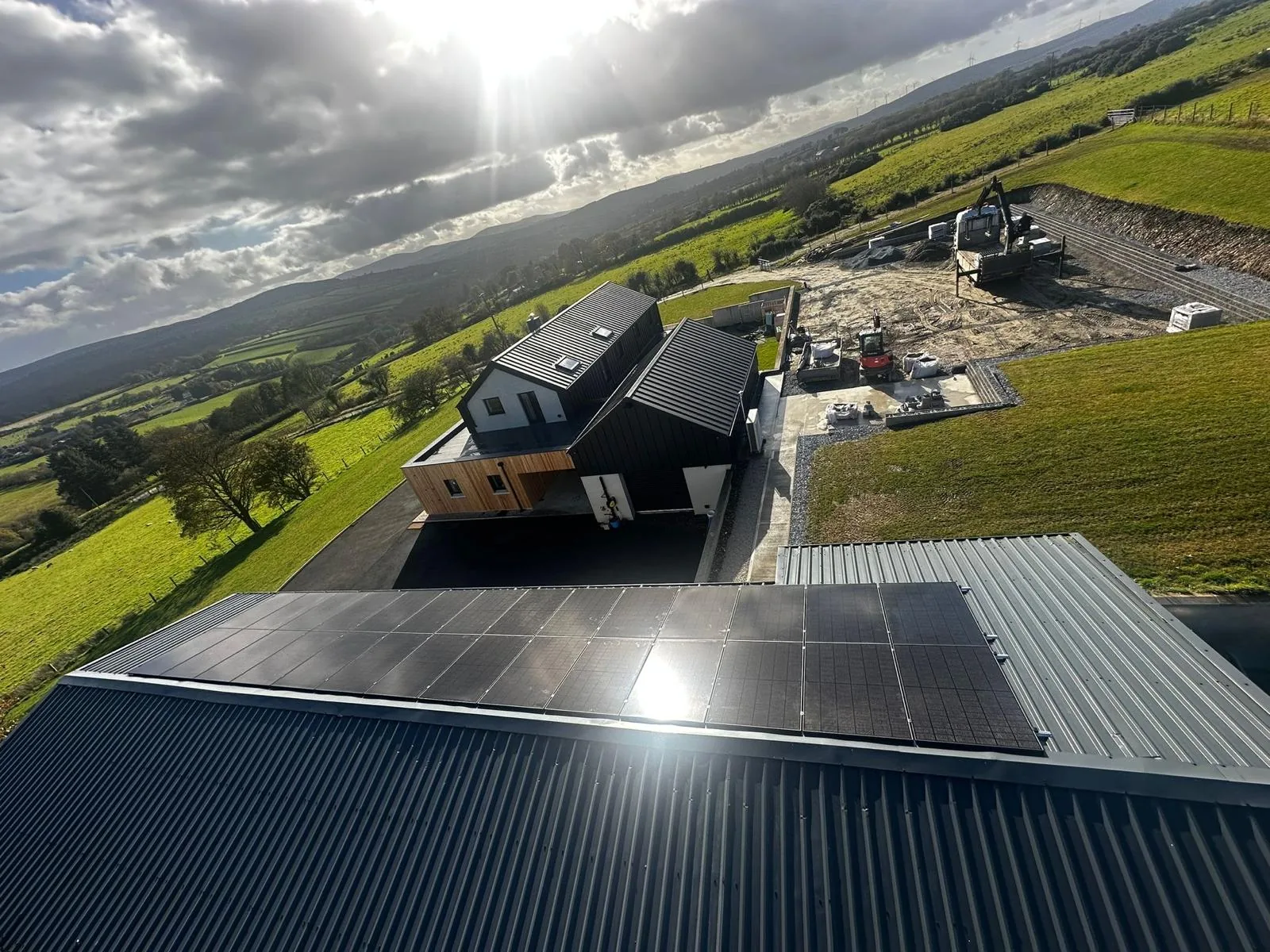 Aerial view of black solar panels on a corrugated farm shed roof overlooking fields