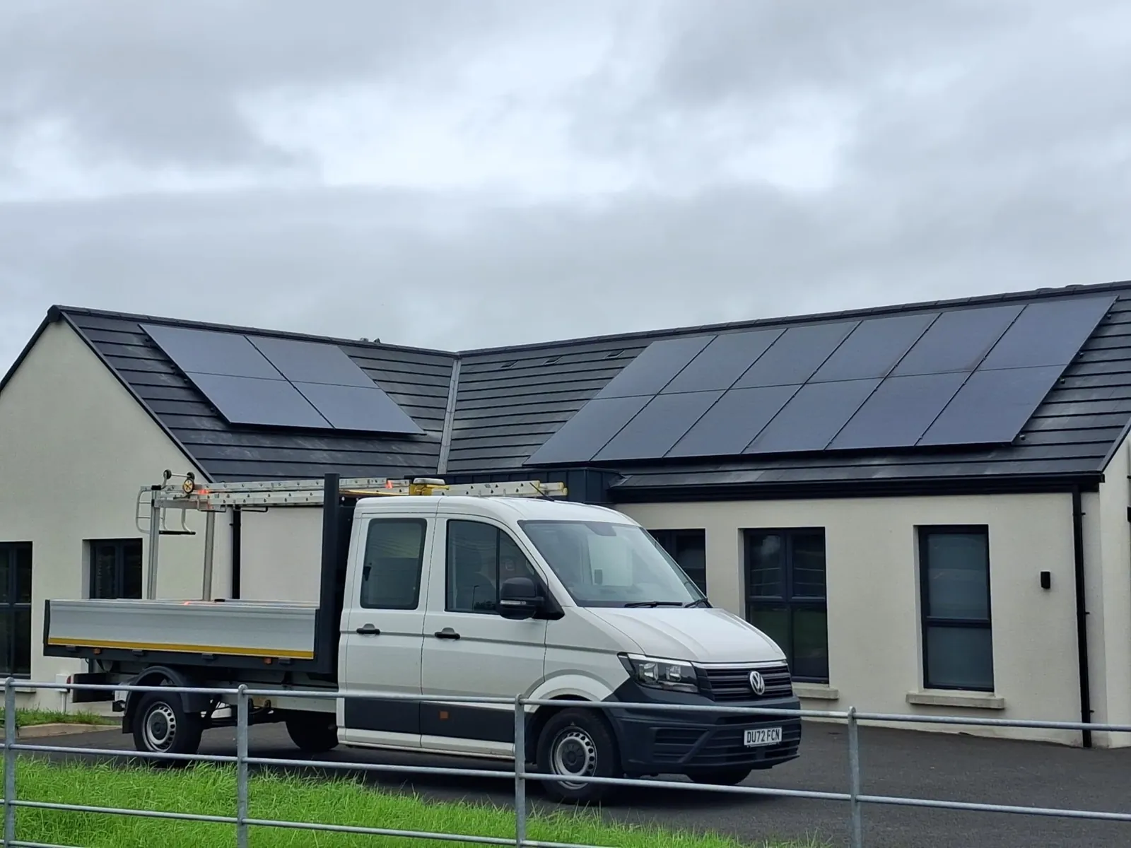 Black solar panels on two roof sections of a modern bungalow, with a Solar Power NI van in front