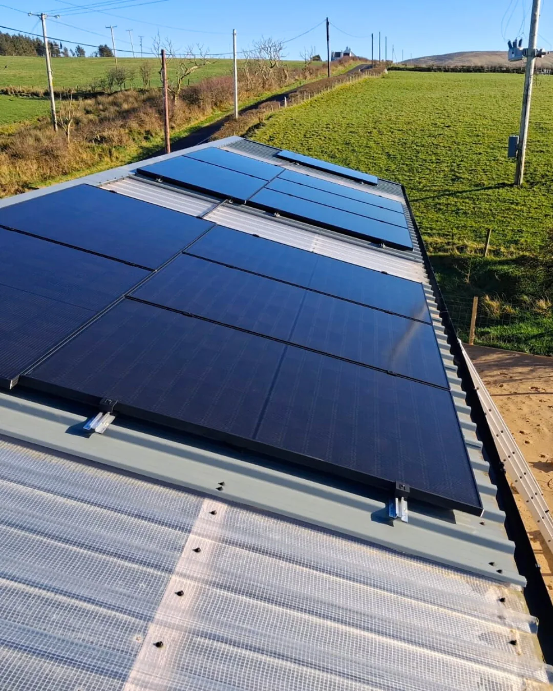 Close-up of black solar panels fixed to a corrugated farm outbuilding roof with roof lights