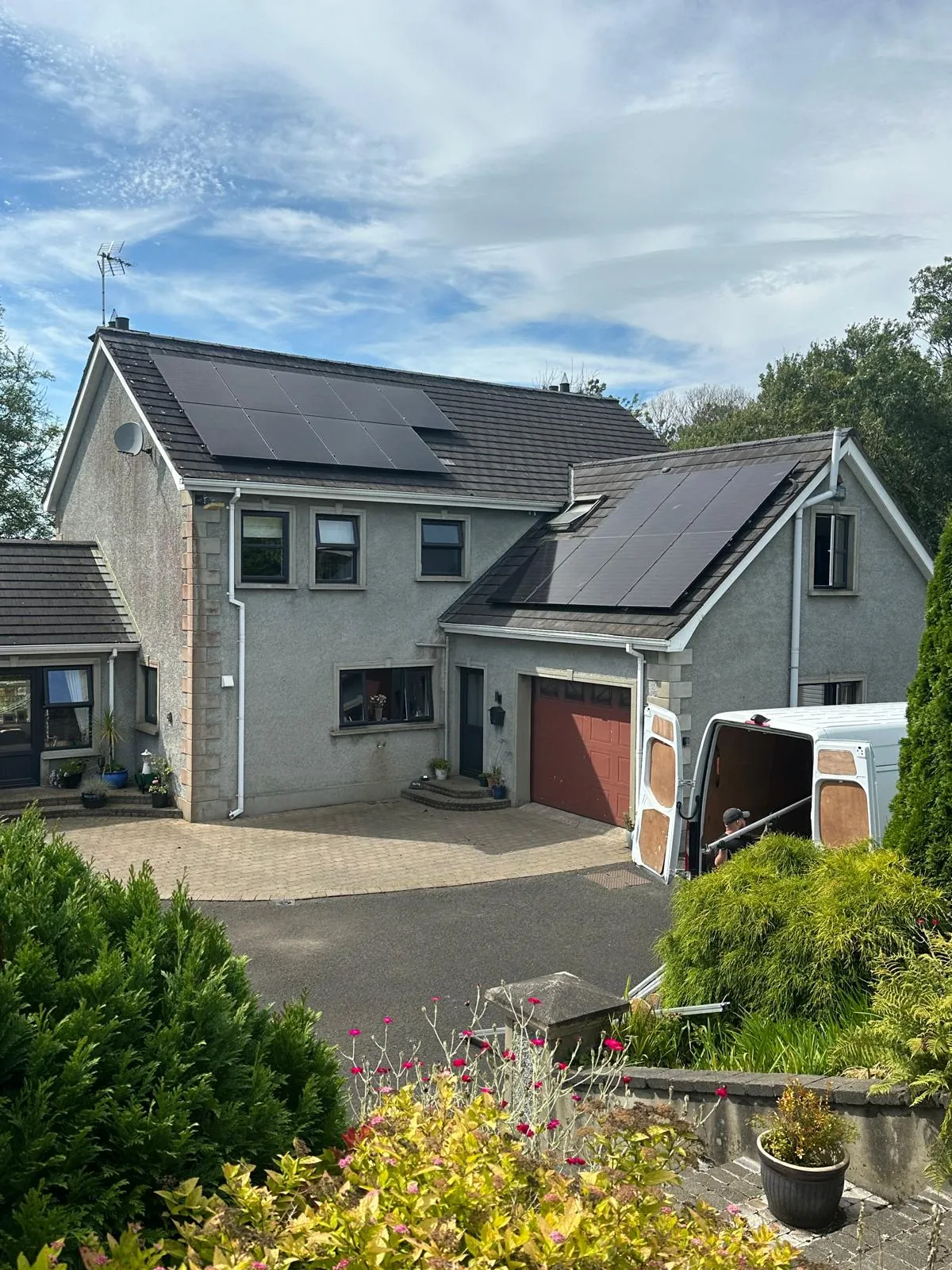 Black solar panels on the main roof and garage roof of a detached house